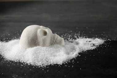 Sağlıksız beslenme kavramını sembolize eden tahta bir yüzey üzerindeki kafatası şekilli şeker yığını..
