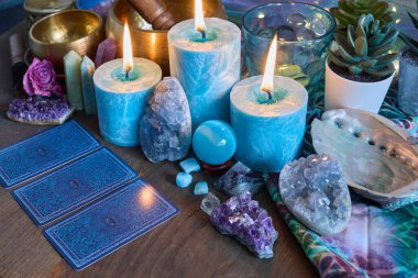 Tahta bir yüzey üzerinde mumlar, kristaller ve tarot kartları mistik bir hava yaratıyor..