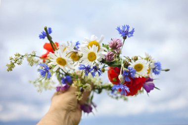 Bulutlu bir gökyüzüne karşı tutulan canlı bir buket kır çiçeği..