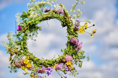 Havada asılı renkli bir çiçek çelengi kabarık bulutlu mavi bir gökyüzünün arka planına karşı.