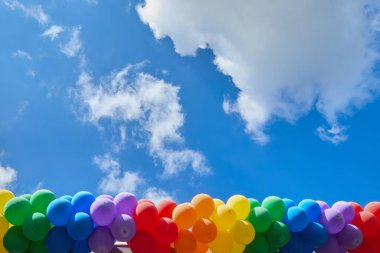 Canlı bir dizi renkli balon, dağınık beyaz bulutlarla parlak mavi bir gökyüzüne vuruyor..