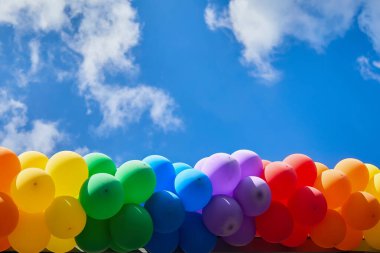 Canlı bir dizi renkli balon, kabarık bulutlu açık mavi bir gökyüzüne doğru süzülür..