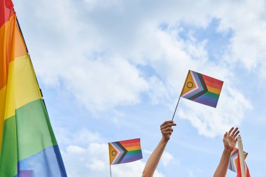 Mavi gökyüzünde bulutlu bayrakları tutan eller