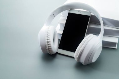 White headphones, smartphone, and stacked books on a sleek grey surface. clipart
