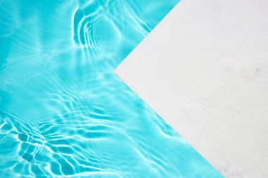 Parlak güneş ışığı altında turkuaz su ve beyaz platformlu minimalist havuz kenarı tasarımı.