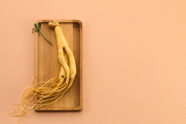 Taze ginseng kökü, şeftali arka planına karşı ahşap bir tahtaya yerleştirilmiş..