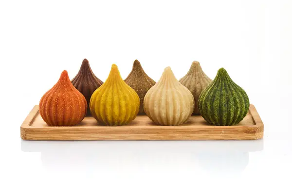 stock image An array of vibrant, traditional Modak sweets in various colors, presented on a wooden tray.