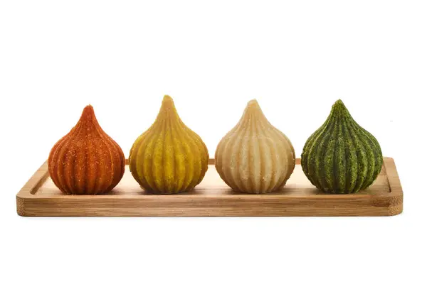 stock image An array of vibrant, traditional Modak sweets in various colors, presented on a wooden tray.