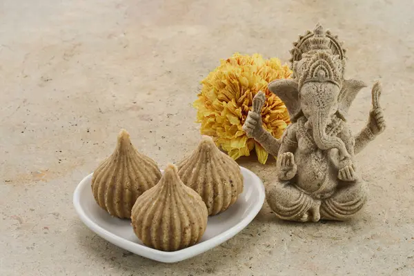 stock image Ganesha statue with modak sweets and a yellow flower on a neutral background.