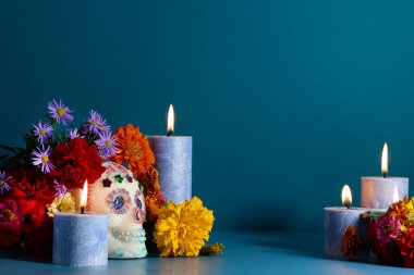 Mavi arka planda mumlar ve dekoratif kafatası ile renkli çiçek aranjmanı.
