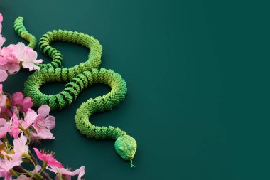 Pembe çiçeklerin yanında duran canlı yeşil bir yılan..