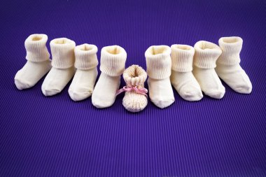 Rows of baby socks and a single pair with a bow on a purple backdrop. clipart