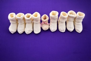 Rows of baby socks and a single pair with a bow on a purple backdrop. clipart