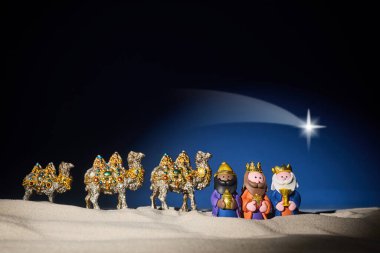 A festive scene featuring three colorful wise men figurines with camels on a sandy landscape under a starry night.