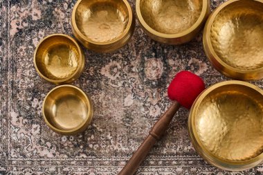 Pirinç kaseler kırmızı bir tokmakla desenli bir kilimin üzerinde.