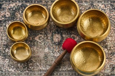 Kalıplı bir halının üzerinde kızıl başlı tokmak olan pirinç kaseler koleksiyonu..