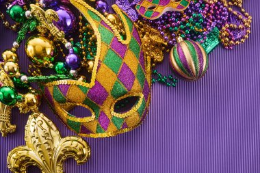 Renkli Mardi Gras maskesi ve parlak mor arkaplanda boncuklar..