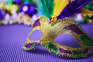 Mor arka planda tüyleri olan renkli Mardi Gras maskesi, şenlik ve canlılığı somutlaştırıyor..