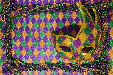 Canlı bir Mardi Gras maskesi soytarı desenli arka planda renkli boncuklarla çevrili..