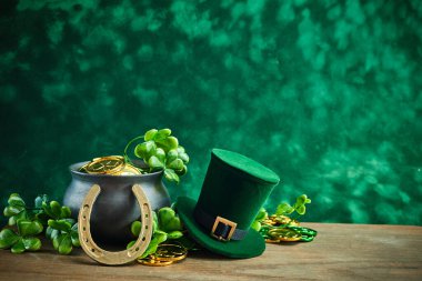 A festive setup with a pot of gold, leprechaun hat, horseshoe, and shamrocks on a wooden surface. clipart