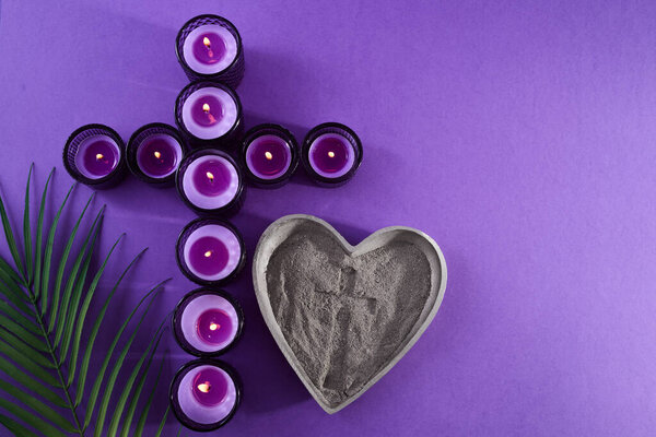 A cross of candles, palm leaves, and ash in a heart shape, on a purple background.