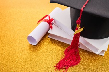 Mezuniyet şapkası, diploma ve altın arkaplan kitapları..