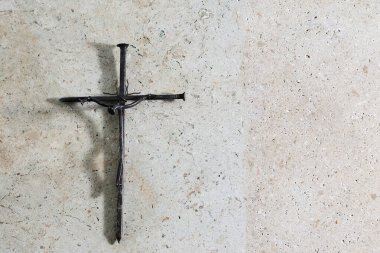 Çivilerden yapılmış metal bir haç. Minimalist bir tasarıma sahip desenli bir taş zemine sabitlenmiş..