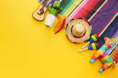Sombrero, marakas, gitar, kaktüs ve sarı arka planda renkli battaniye ile Meksika temalı canlı bir düzenleme..