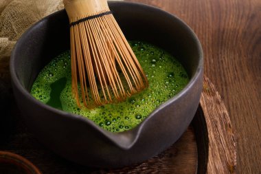 Geleneksel bir kibrit çırpma ve kase ahşap bir masada, canlı yeşil çay sergiliyor..