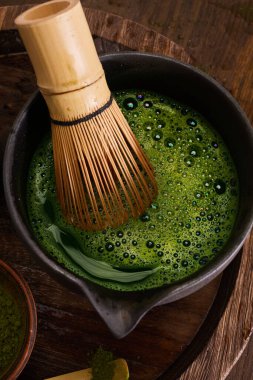 Bambu çırpıcı, ahşap bir yüzeyde, koyu renkli bir kasede canlı yeşil kibrit hazırlamak için kullanılır..