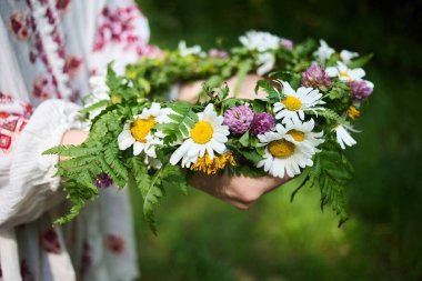 Yeşillik ve papatyalarla dolu canlı bir çiçek çelengi, yemyeşil bir arka planda tutan bir el..