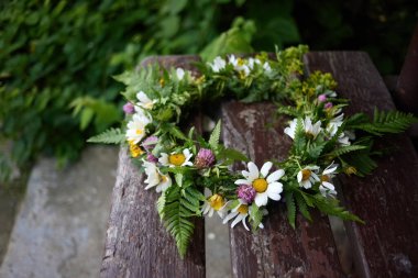 Kırsal bir ahşap bankta yeşil papatyalar ve eğreltiotlarıyla el yapımı bir taç..