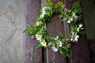 Çiçekli bir papatya tacı, yemyeşil bir zemine dayanan bir kayanın üzerinde duruyor..