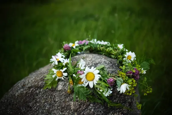 Çiçekli bir papatya tacı, yemyeşil bir zemine dayanan bir kayanın üzerinde duruyor..