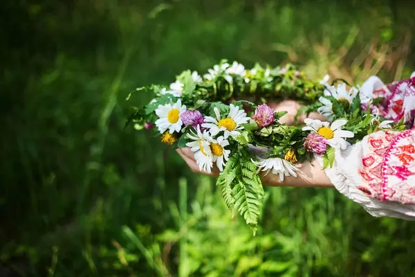 Yeşillik ve papatyalarla dolu canlı bir çiçek çelengi, yemyeşil bir arka planda tutan bir el..