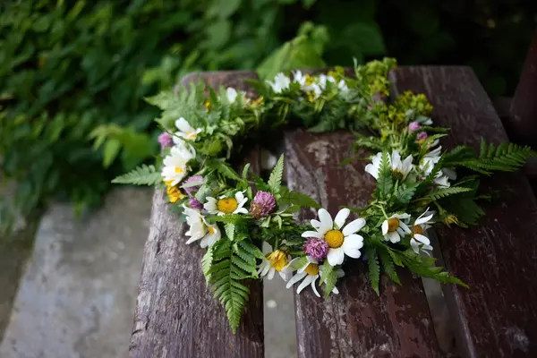 Kırsal bir ahşap bankta yeşil papatyalar ve eğreltiotlarıyla el yapımı bir taç..