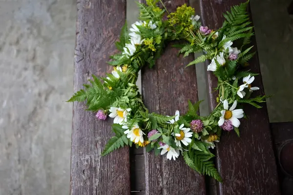 Çiçekli bir papatya tacı, yemyeşil bir zemine dayanan bir kayanın üzerinde duruyor..