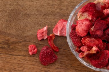 Ahşap bir masanın üzerinde canlı kırmızı, dondurulmuş çilek dolu bir cam kase..