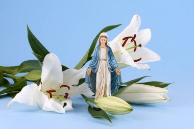 Sakin mavi arka planda zarif beyaz zambaklar arasında dinsel bir heykel..