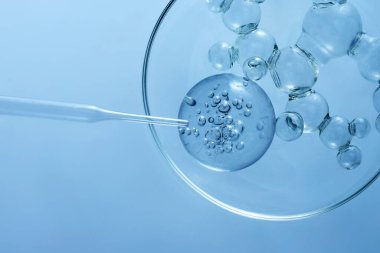 Petri kabında yüzen baloncukların mavi renkli pipetle soyut görüntüsü..