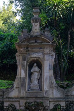 A dilapidated ancient statue in a niche in the park with an inscription in Latin 