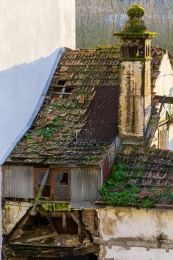 An old abandoned house with a small window, a chimney and a tiled roof and white walls
