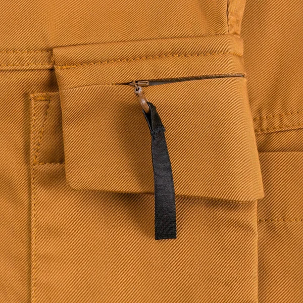 Detail of ocher colored cargo pants. Zipped side pocket with black tab close up