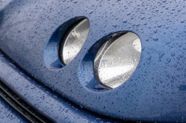 Round blue car headlights covered with drops after rain close up