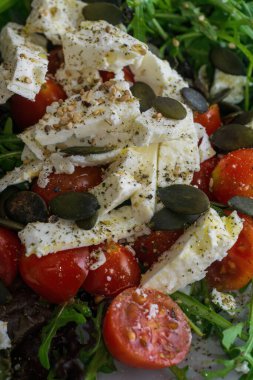 Salad with rucola, feta, cherry tomatoes, pumpkin seeds and sesame on a grey-blue handmade plate close up