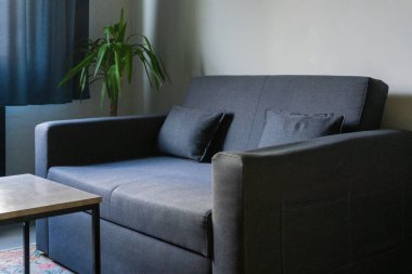 Küvette palmiye ağacının yanında küçük, modern, mavi ve gri bir kanepe ve mermer kapaklı bir çatı katı tarzı masa. Beyaz bir duvarda soyut resim