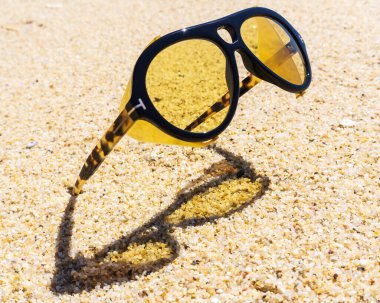 Unusual yellow sunglasses stuck in the sand on the beach close up