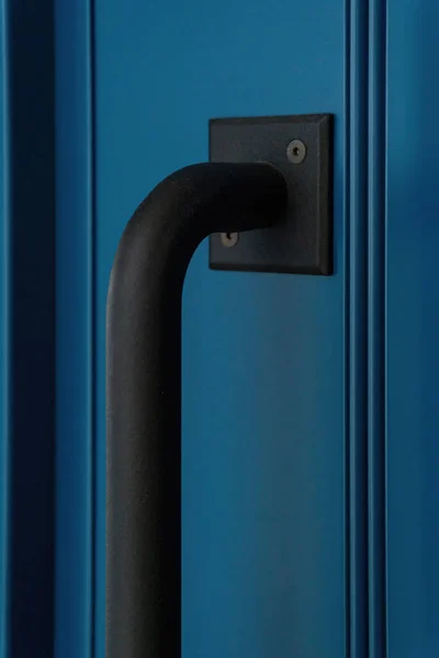 Large black matte metal handle on a blue door close up