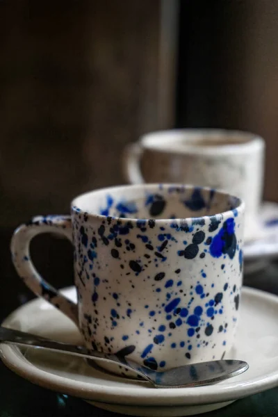 Stock image White coffee cup with blue spots on a saucer with a spoon on a wooden table close up