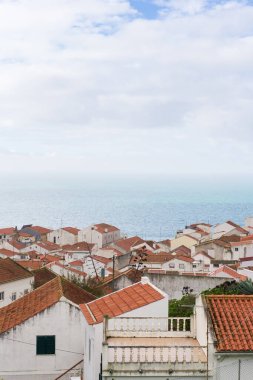 Beyaz evleri ve turuncu kiremitli çatıları olan caddelerin en üst görüntüsü, okyanus üzerinde antik bir Portekiz şehri. Nazare, Portekiz